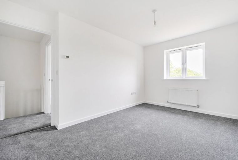 A bedroom with grey carpet, white walls, and a window.