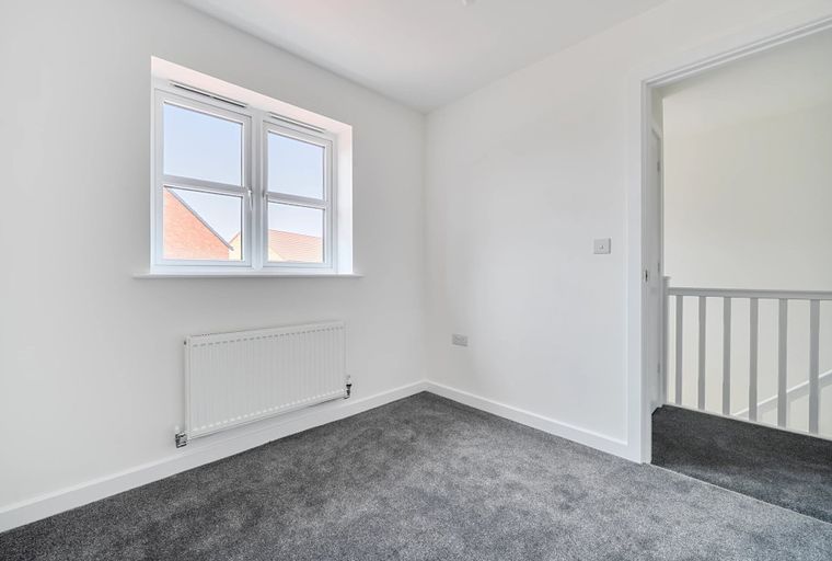 A room with a window, radiator, and a doorway leading to a staircase.