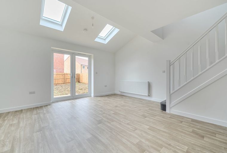 A spacious, empty room with a vaulted ceiling, skylights, double doors, and a staircase.