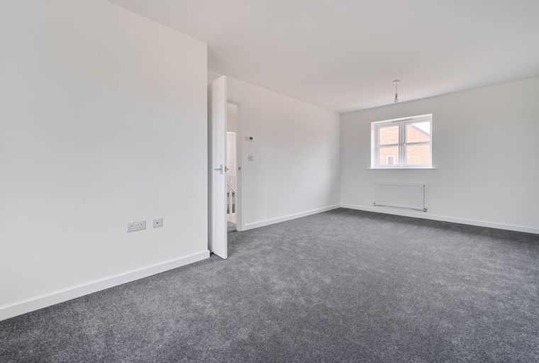 A room with grey carpet, white walls, a window, and a radiator.