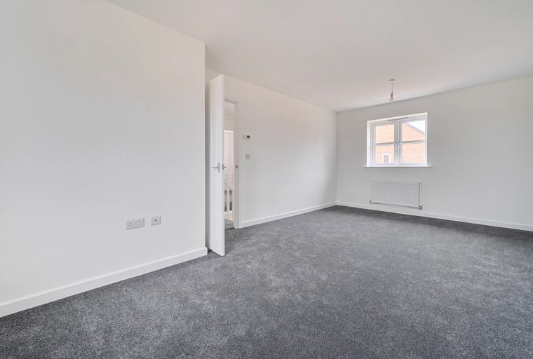 A room with a grey carpet, white walls, a window, and a doorway.