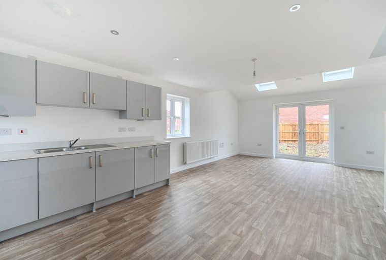 A modern open-plan kitchen and living area with grey cabinets, a sink, and double doors leading to a garden.