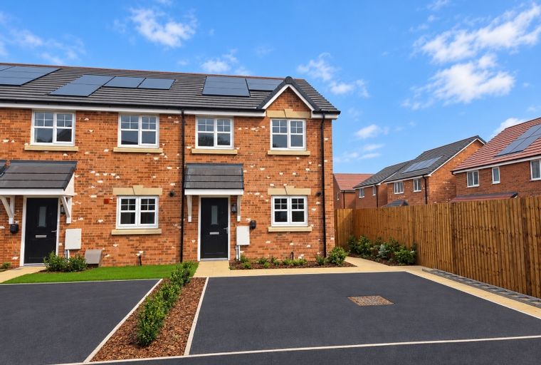 A row of modern brick houses with solar panels on the roof and paved driveways.