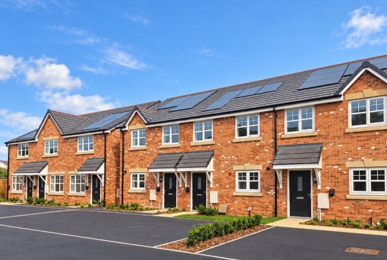 A row of modern brick townhouses with solar panels on the roof under a blue sky.
