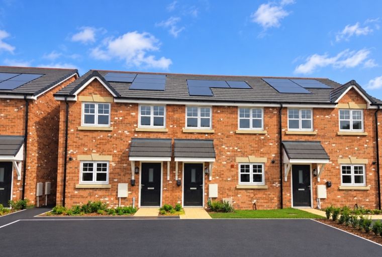 A row of modern brick townhouses with solar panels on the roof under a blue sky.
