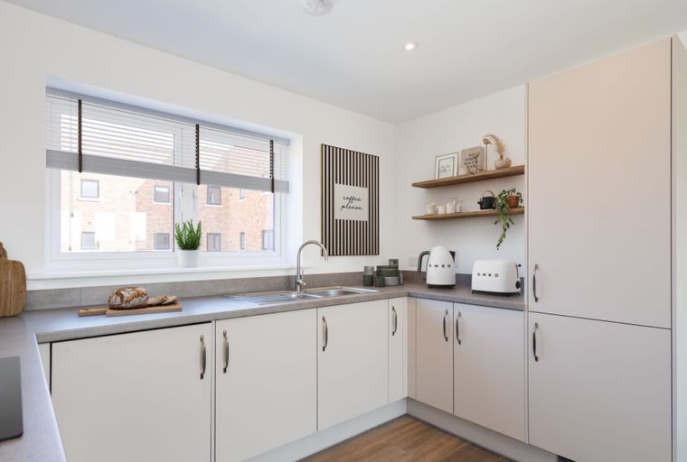 A modern kitchen with cream cabinets, a grey countertop, and a large window.