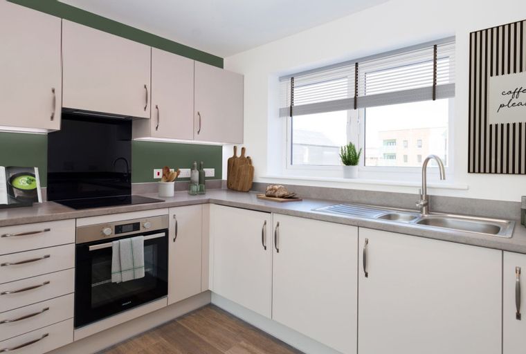 A modern kitchen with light-colored cabinets, a black backsplash, an oven, and a sink.