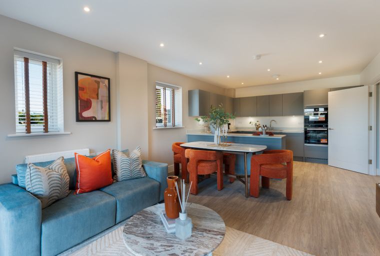A living room and kitchen area with a blue sofa, orange chairs, and a kitchen island.