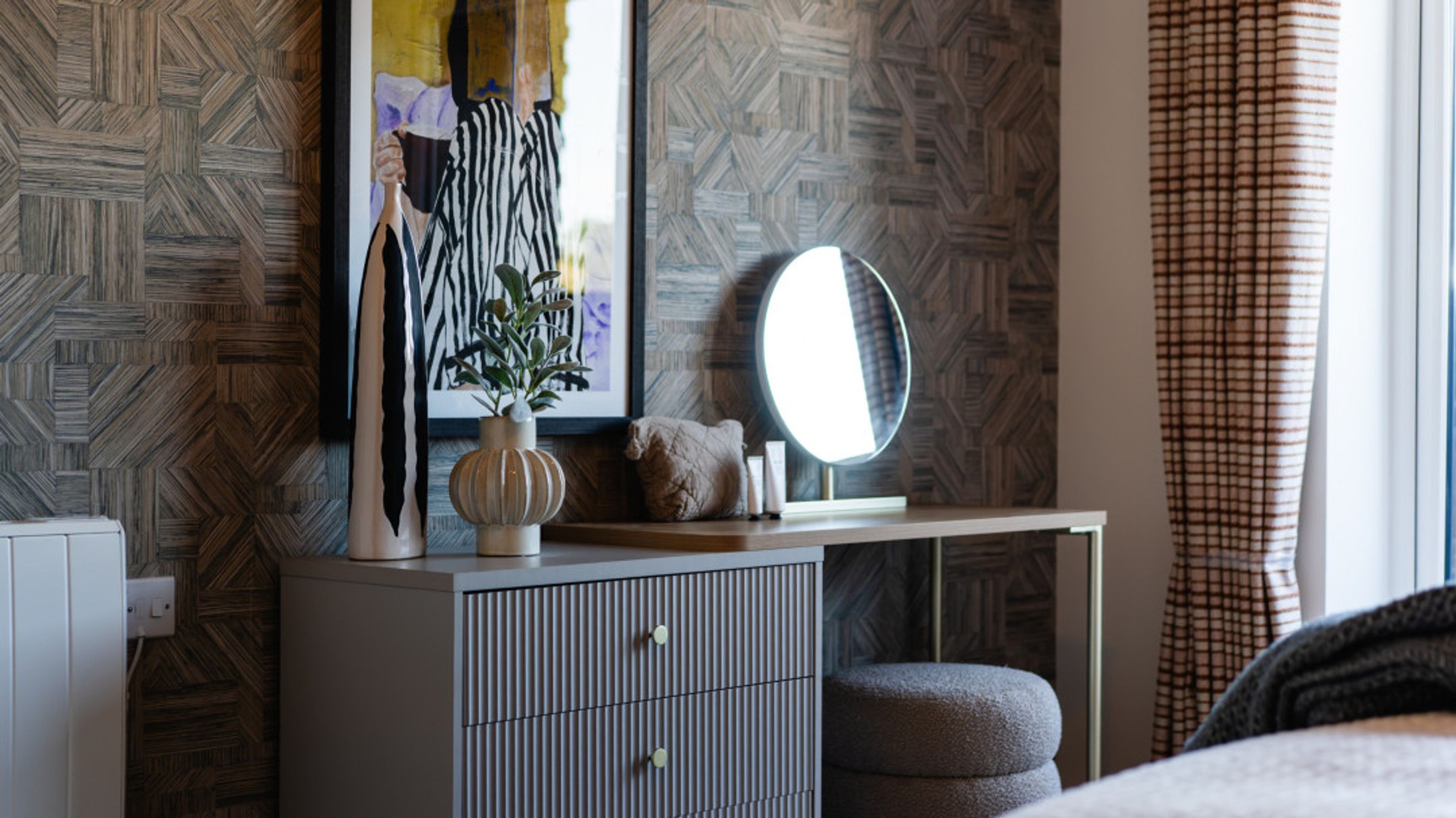 A dressing area with a dresser, vanity table, and lighted mirror.