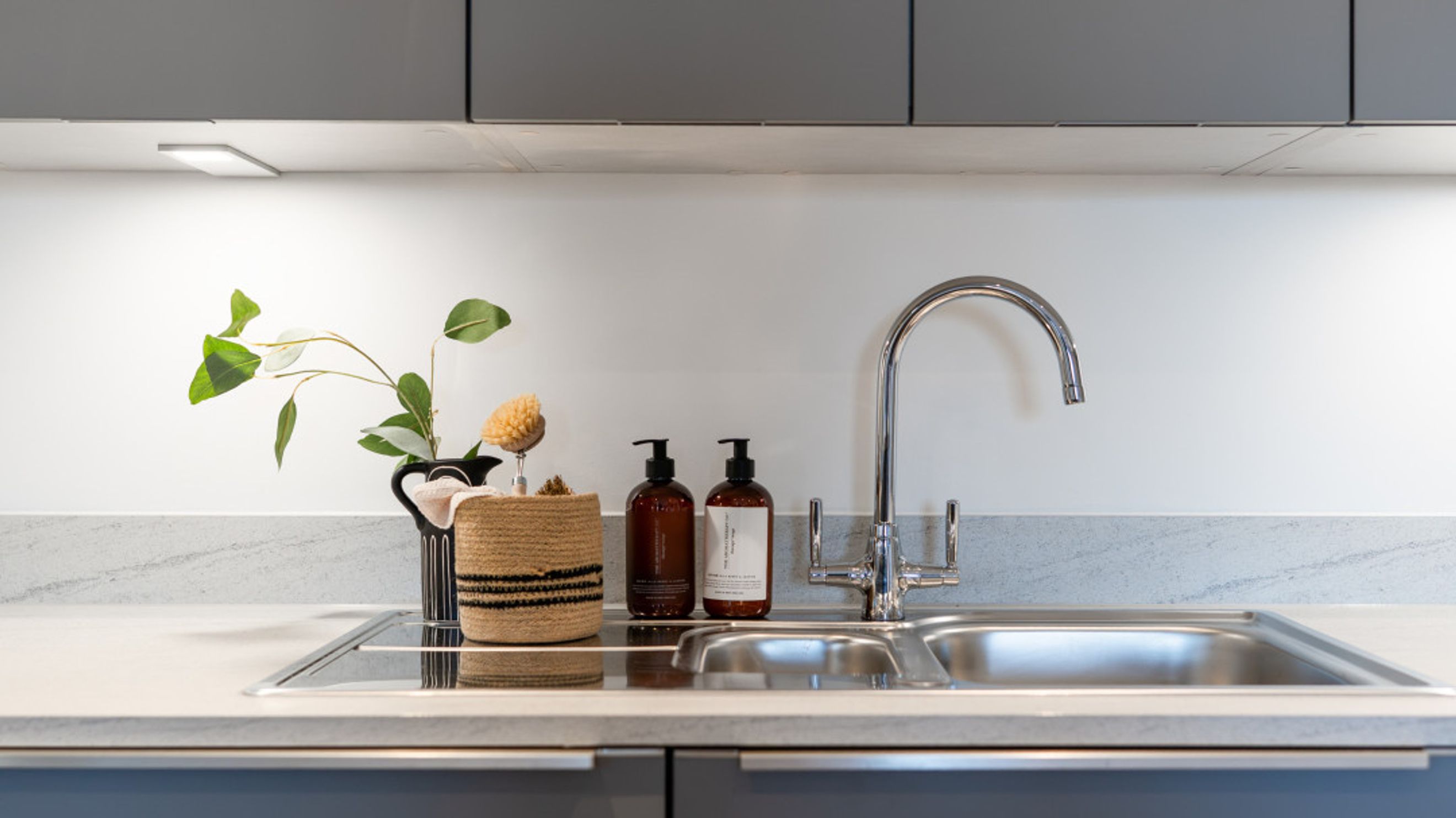 A kitchen sink with a faucet, soap dispensers, and a decorative basket.