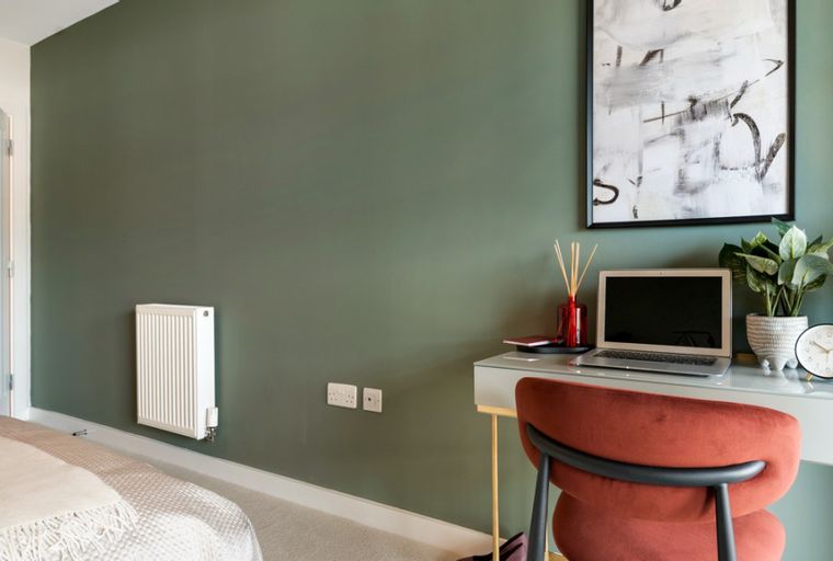 A bedroom with a desk, laptop, chair, and radiator.