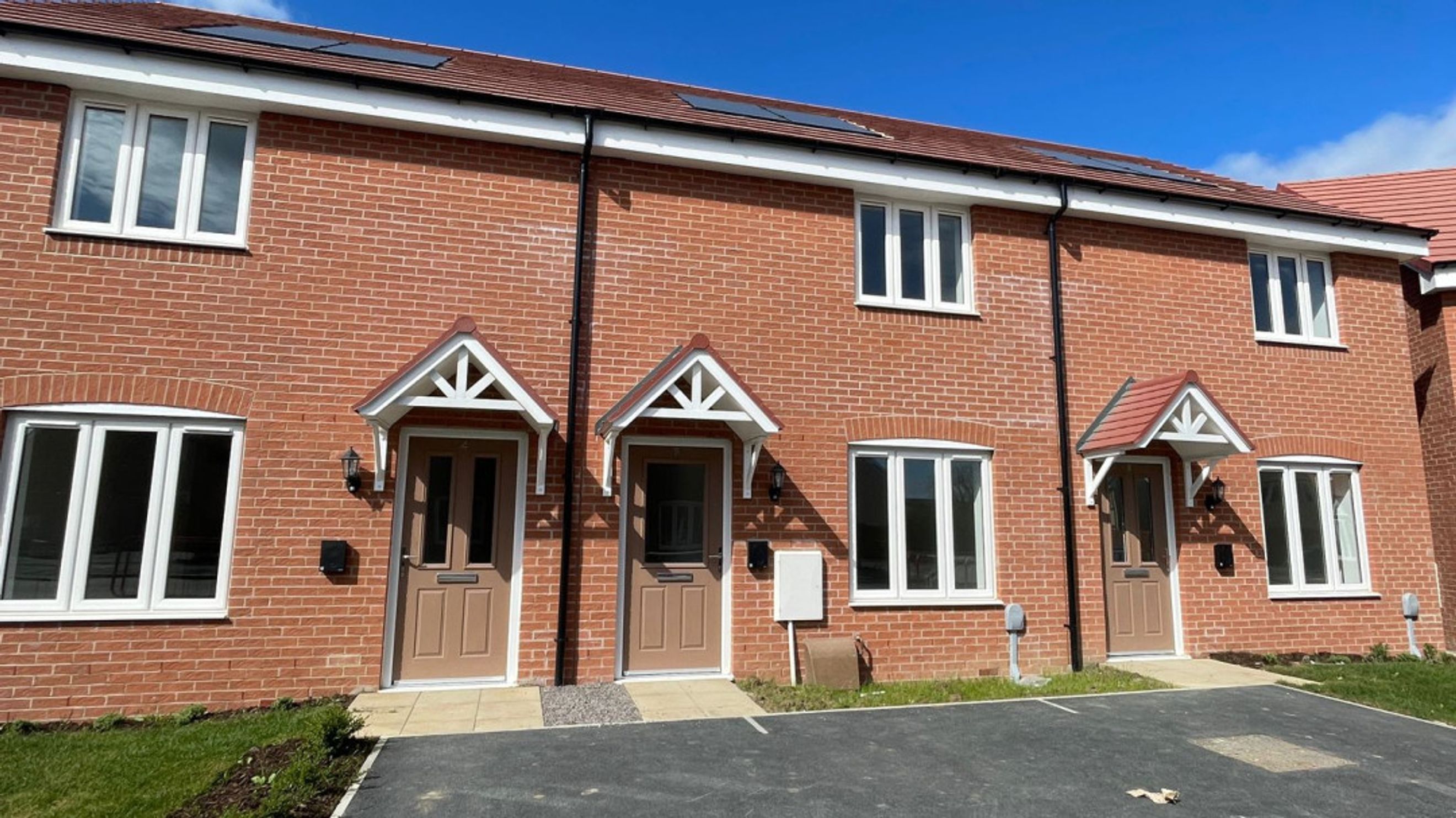 A row of red brick townhouses with white-framed windows and brown doors under a tiled roof.