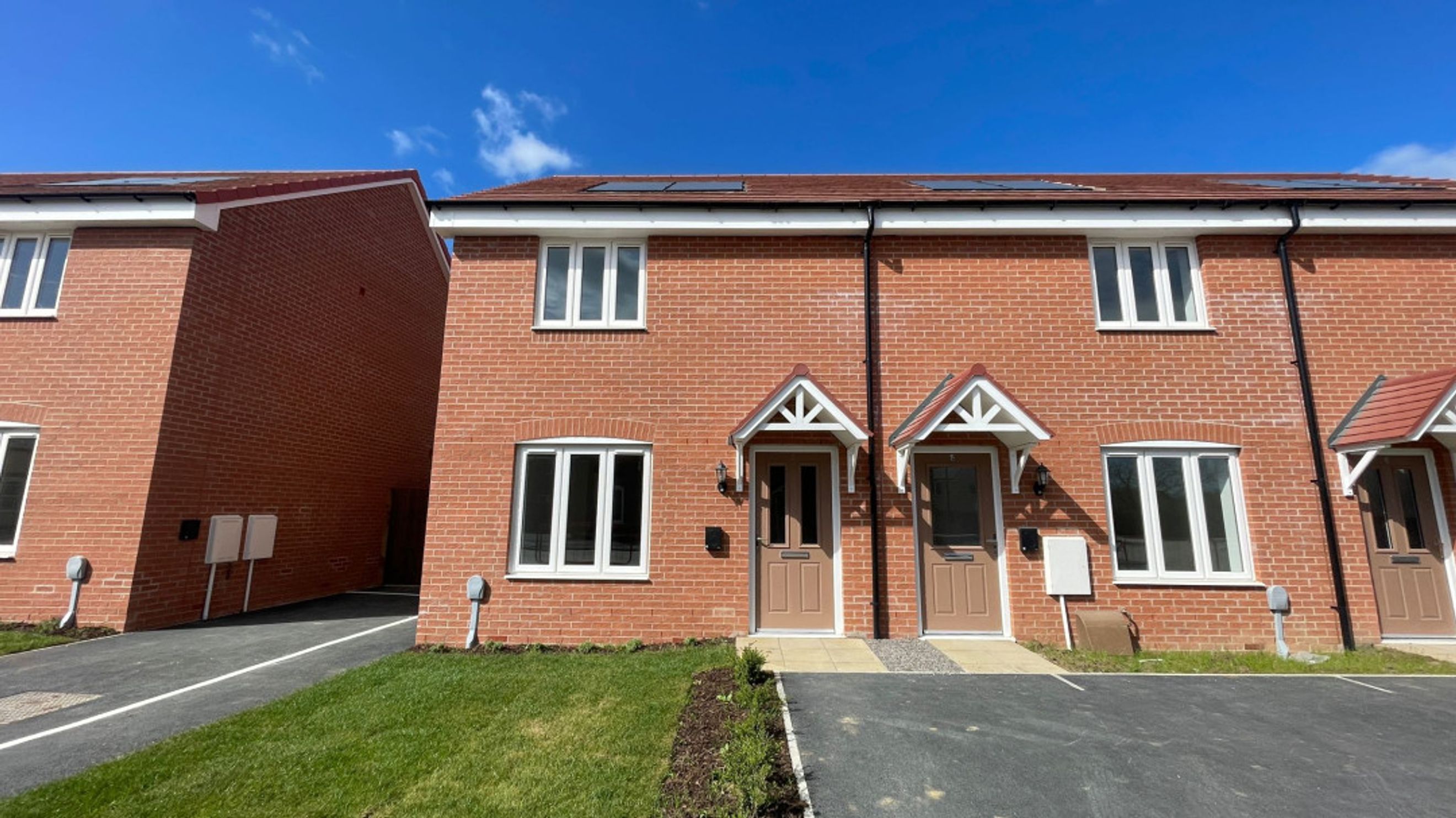 A row of brick townhouses with white windows and brown doors under a blue sky.