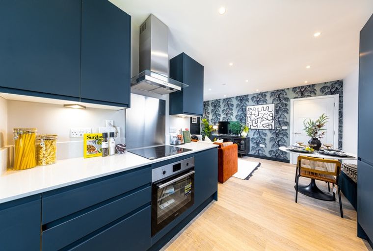 A modern kitchen and living area with navy blue cabinets, a stovetop, an oven, and a dining table.