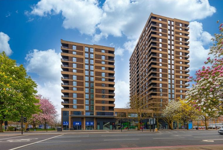 A modern apartment complex with two tall buildings, balconies, and ground-floor retail spaces.