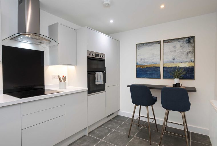 A modern kitchen with grey cabinets, an induction hob, an oven, and a breakfast bar with two stools.