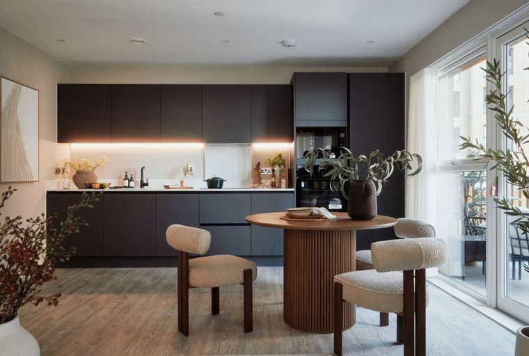 A modern kitchen and dining area with dark cabinets, a round wooden table, and chairs.