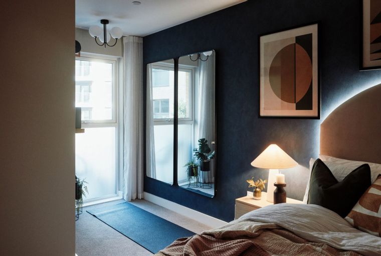 A bedroom with a bed, bedside table, lamp, and mirrors.