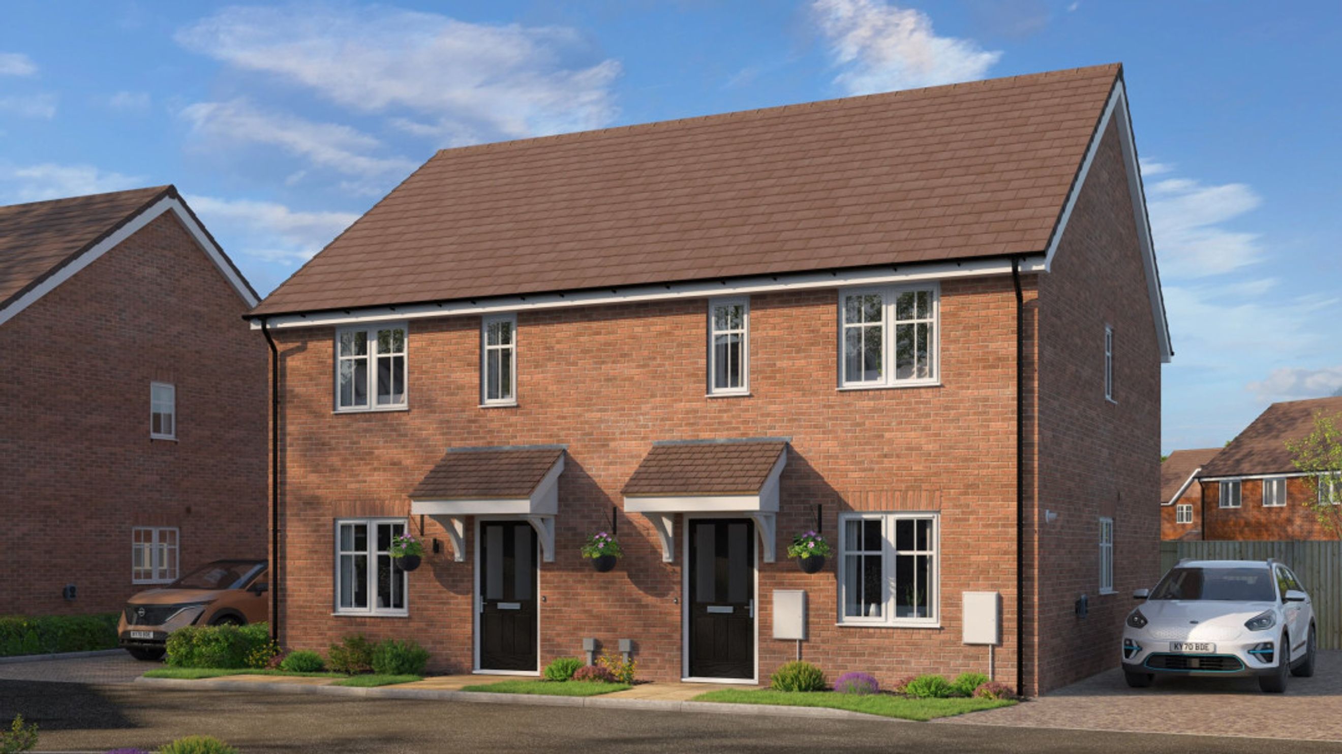 A row of modern semi-detached houses with red brick exteriors and tiled roofs, parked cars, and green landscaping.