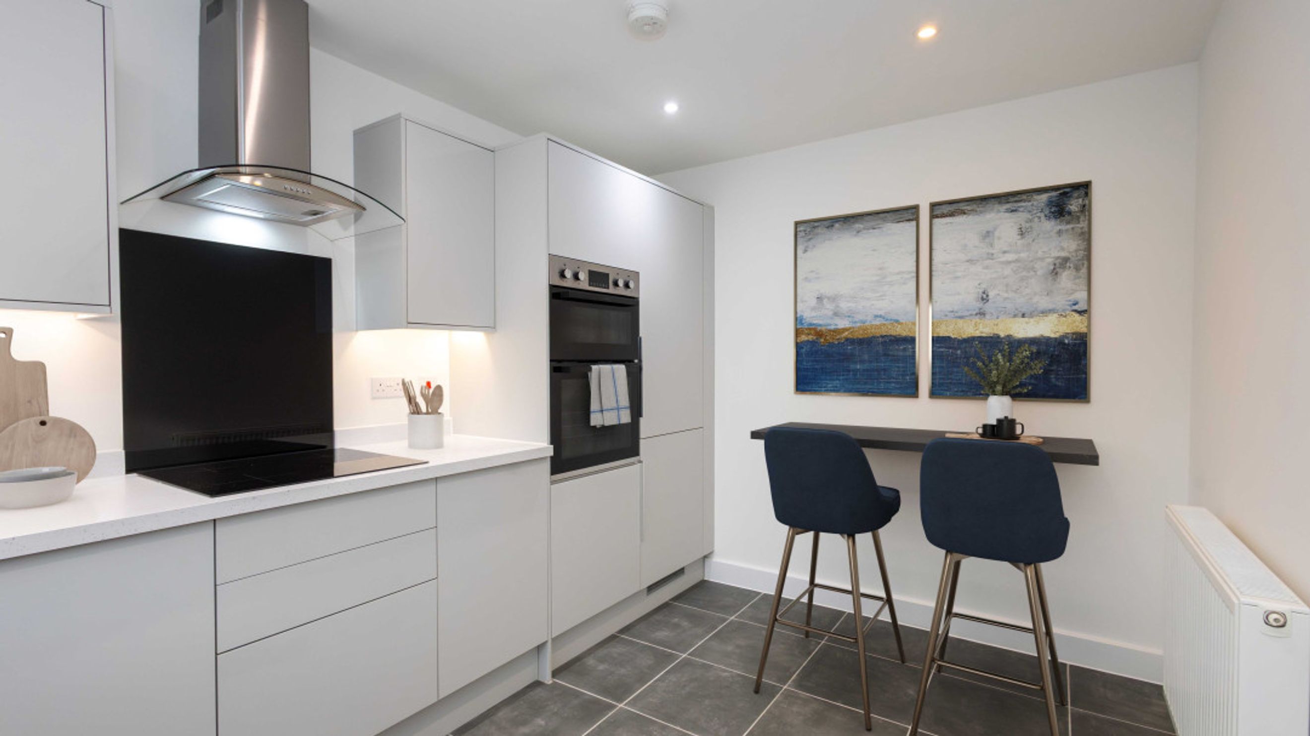 A modern kitchen with grey cabinets, an induction hob, an oven, and a breakfast bar with two stools.