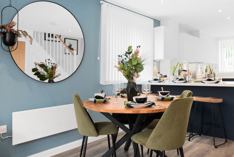 A dining area with a round wooden table, olive green chairs, and a kitchen island.
