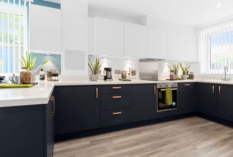 A modern kitchen with dark navy cabinets, white countertops, and copper handles.