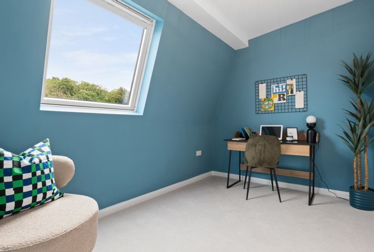A room with a desk, chair, skylight, and armchair.