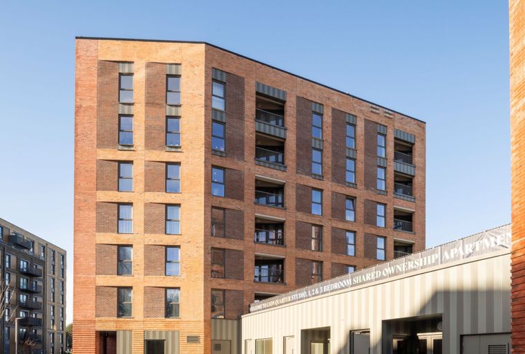 A modern brick apartment building with multiple windows and balconies under a clear blue sky.