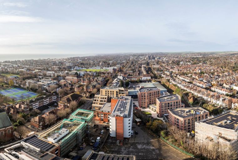An aerial view of a city with residential buildings, parks, and the ocean in the distance.