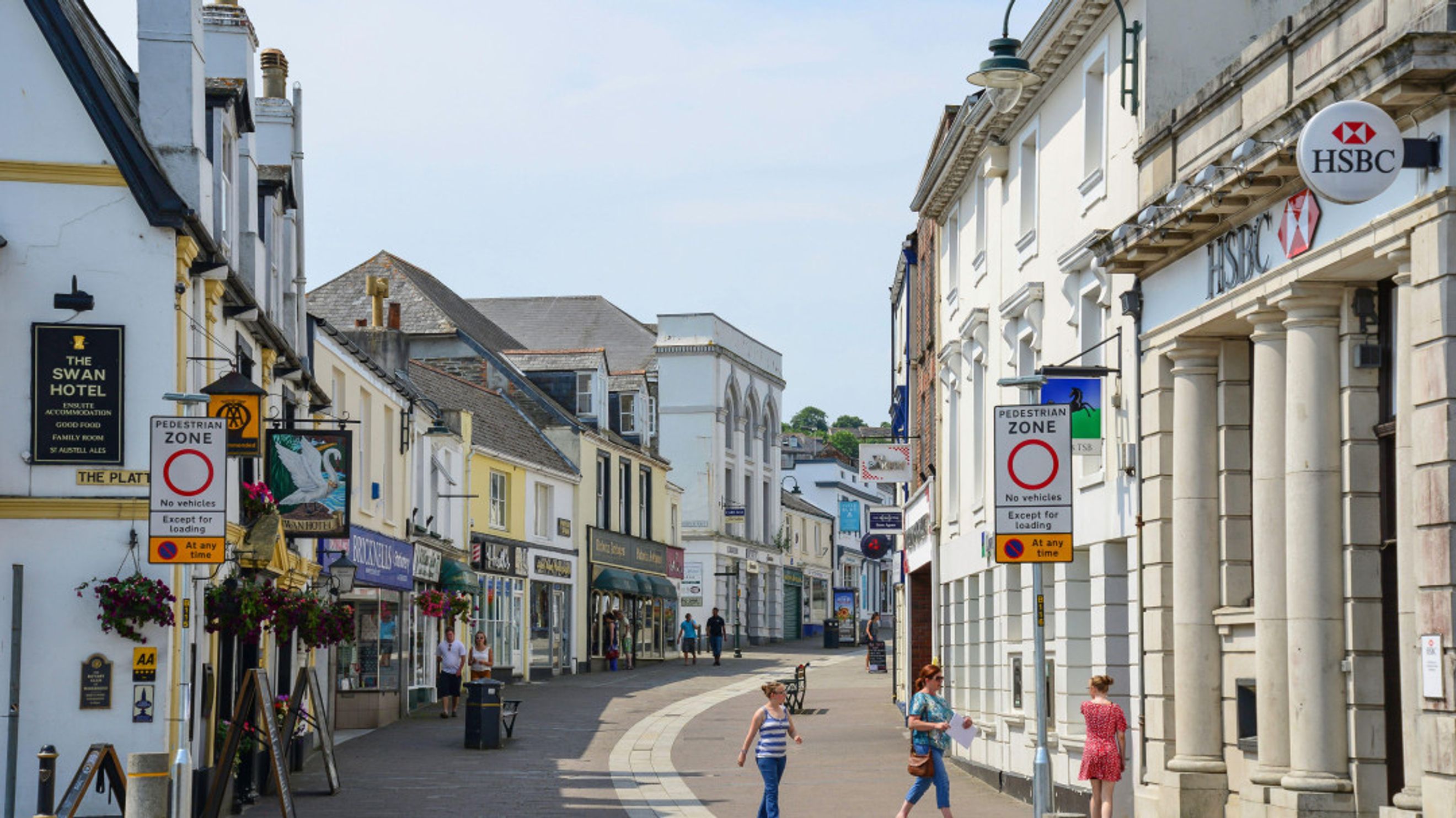 A street scene with shops and a bank on either side, featuring pedestrian zones and signage.