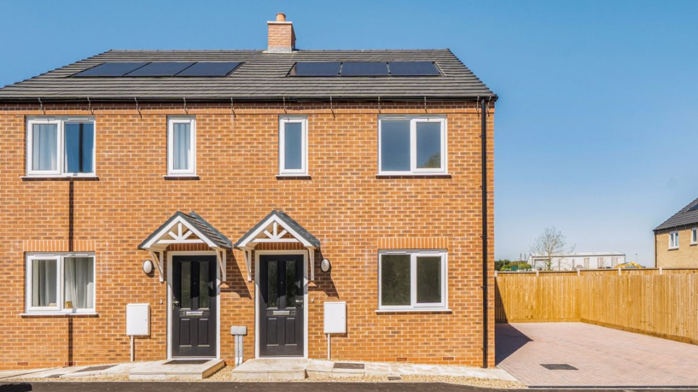 A modern brick semi-detached house with solar panels on the roof and two front doors.