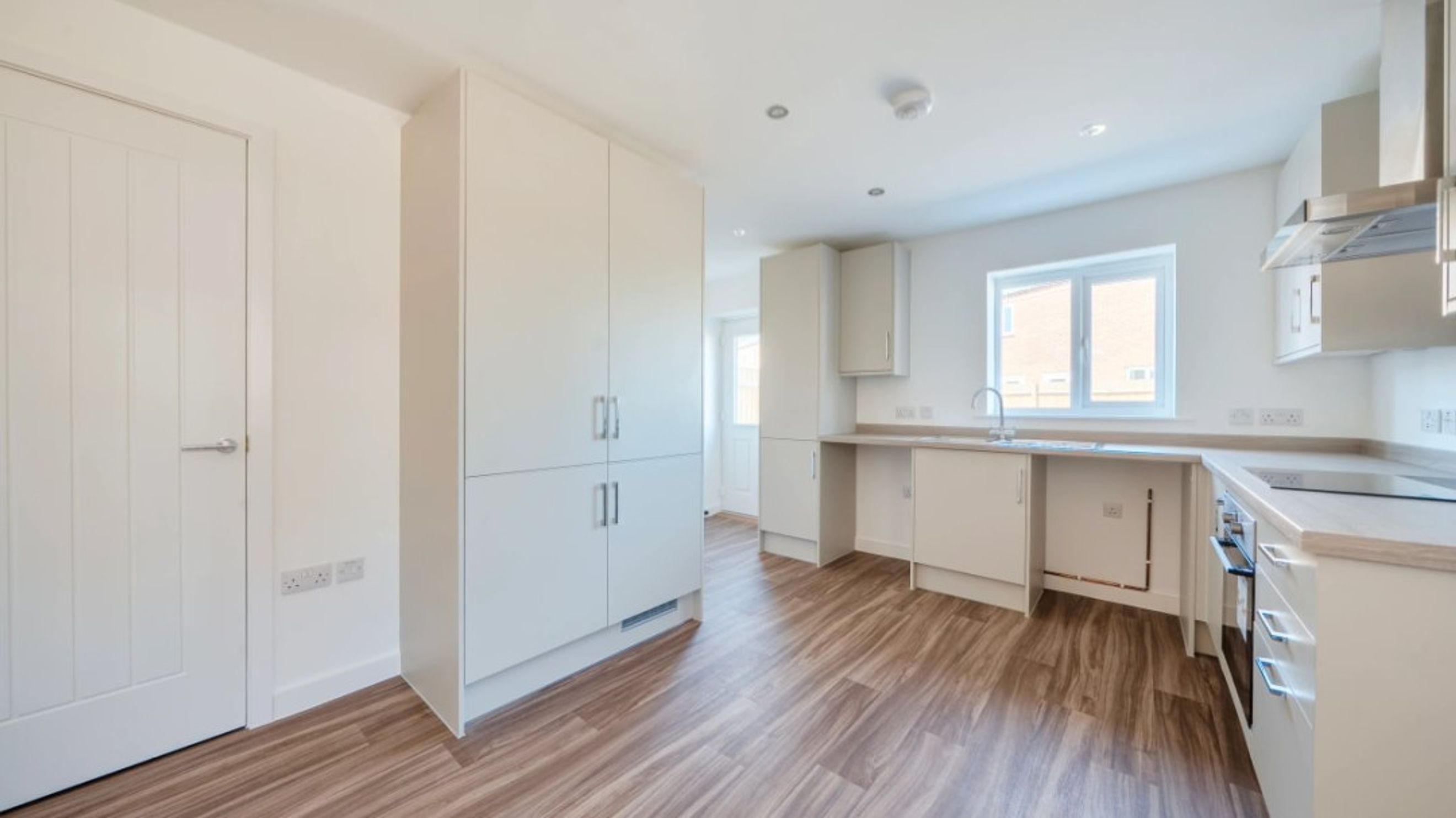 A modern kitchen with white cabinets, a sink, a window, and wood-effect flooring.