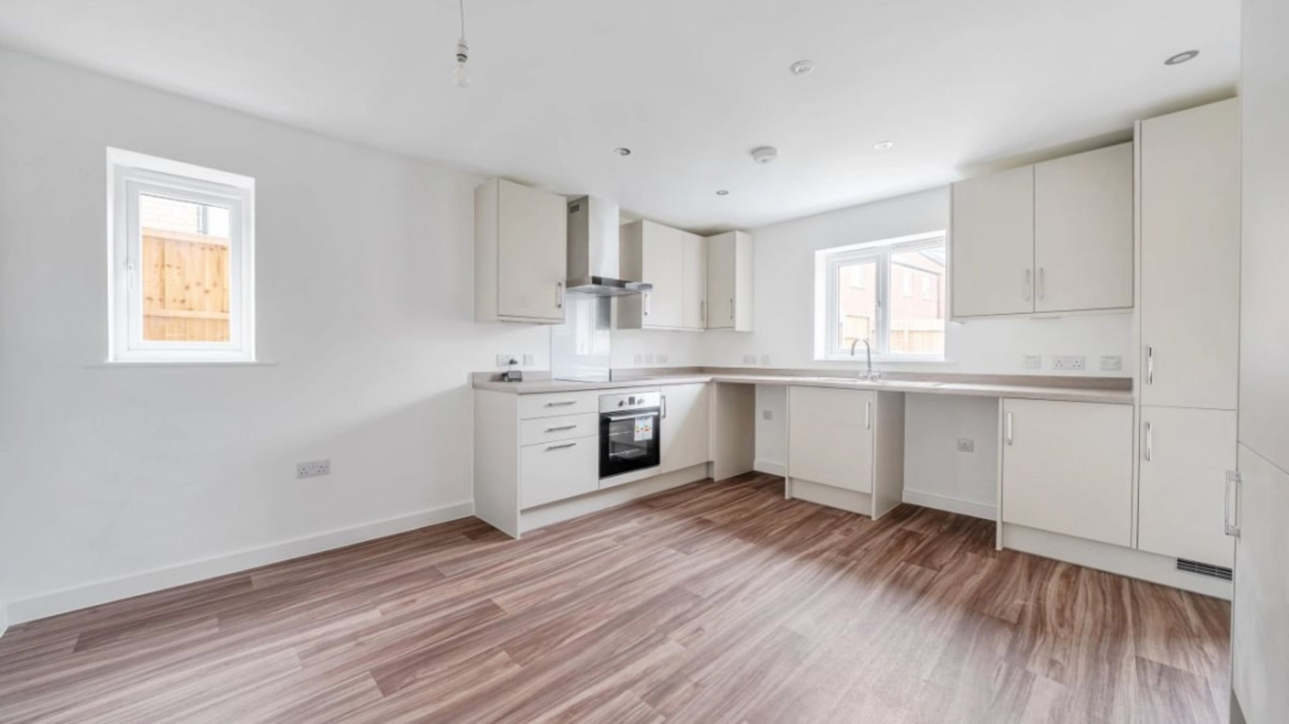 A modern kitchen with white cabinets, an oven, a sink, and wood-effect flooring.