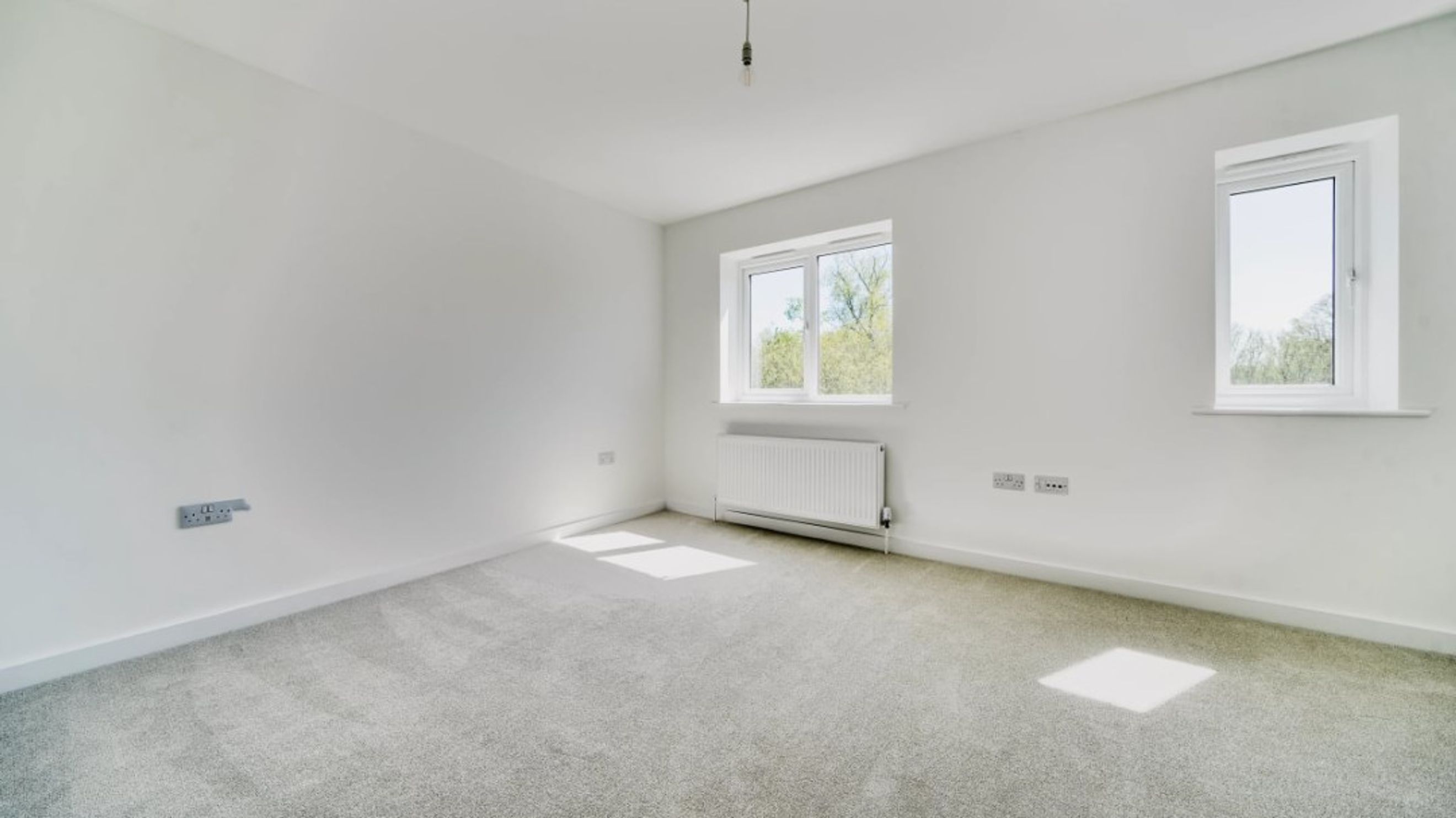 A bedroom with two windows, a radiator, and electrical outlets.