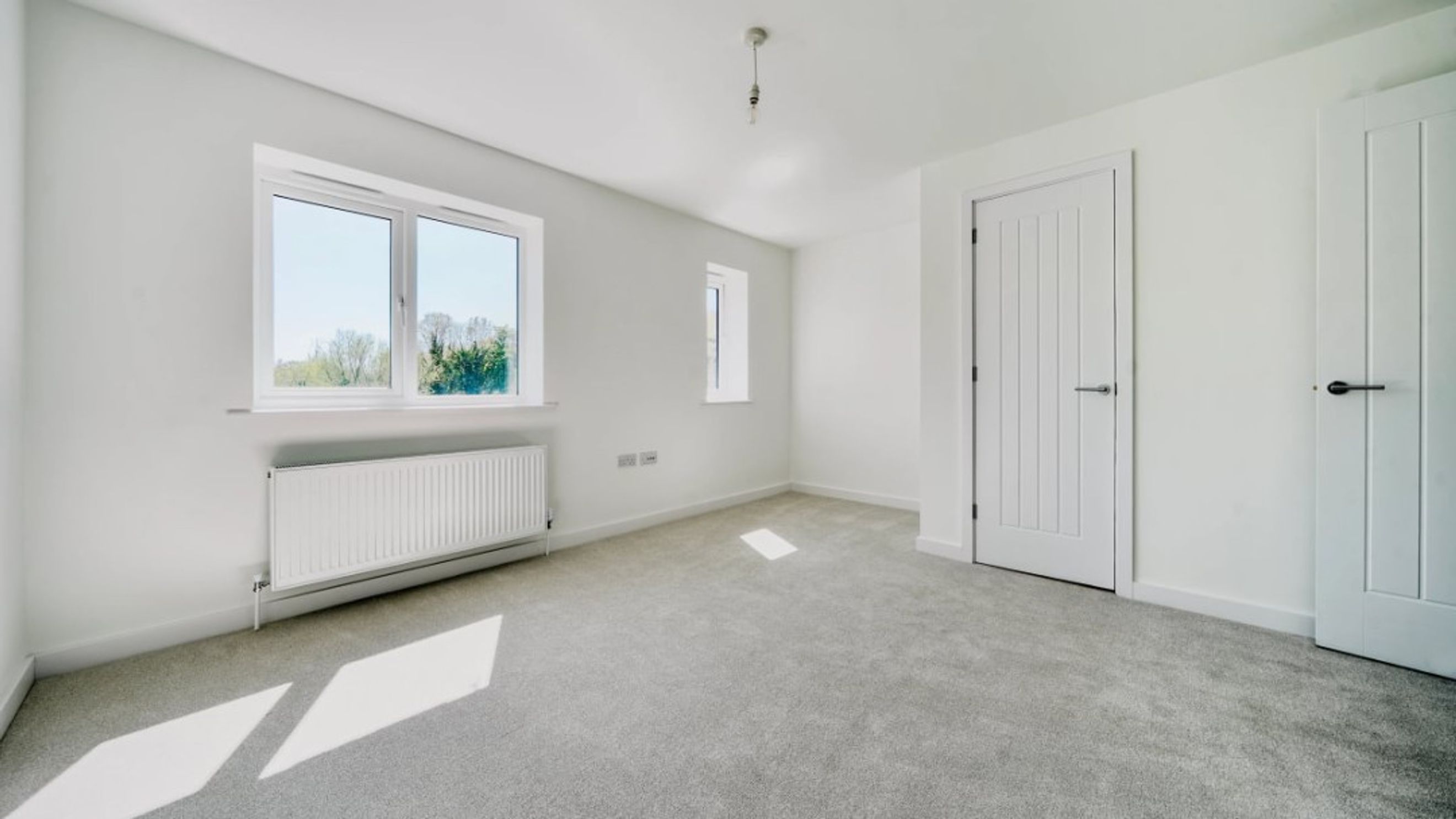 A bedroom with two windows, a radiator, and two doors.