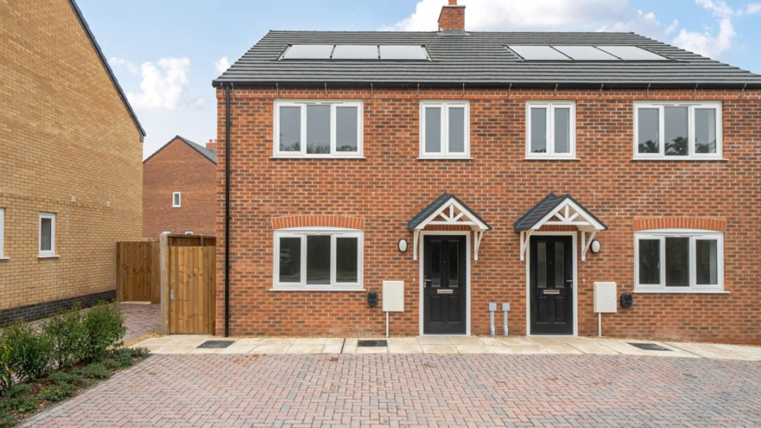 A pair of semi-detached brick houses with black front doors and white windows.