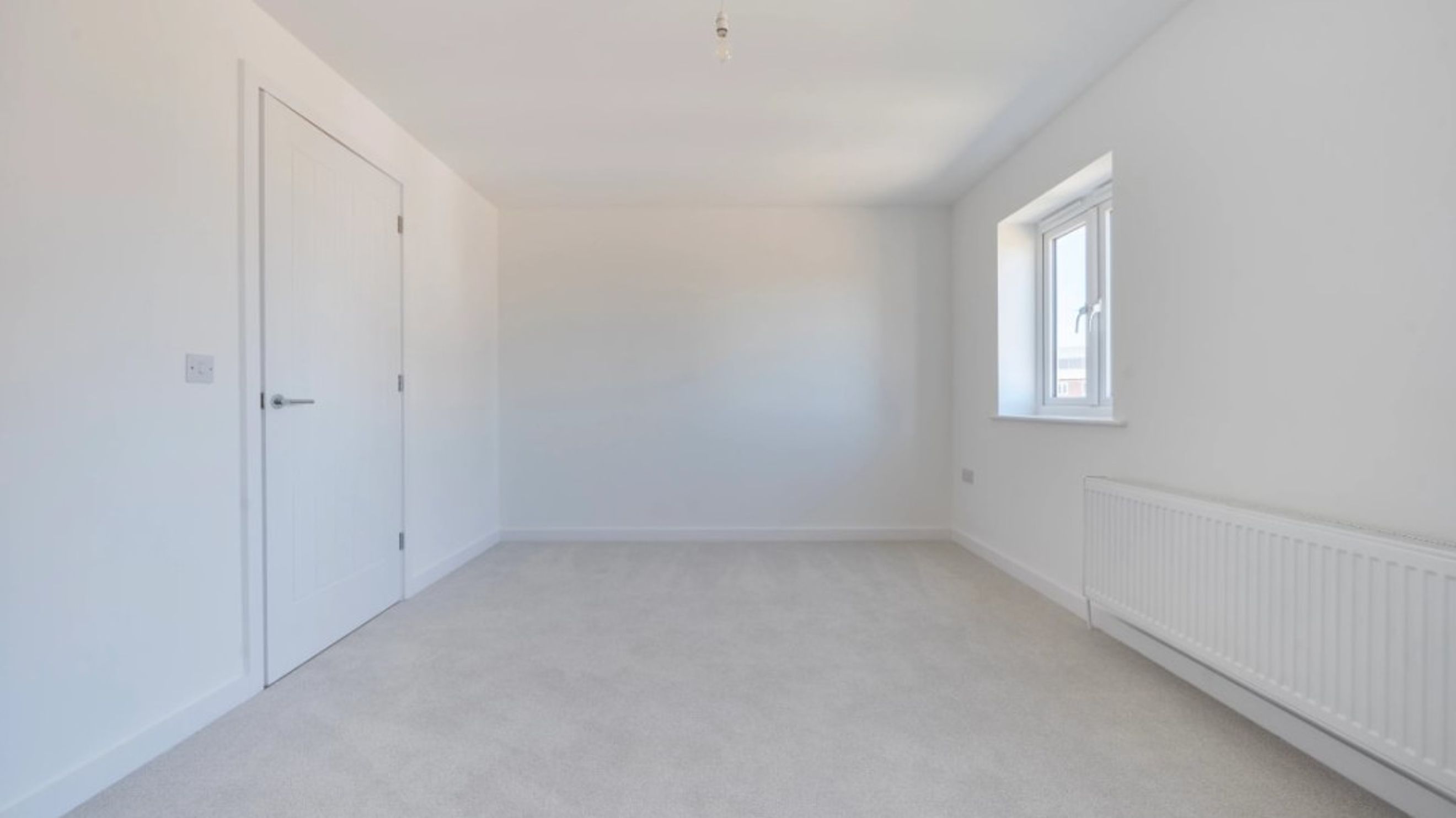 A room with a white door, a window, and a radiator.