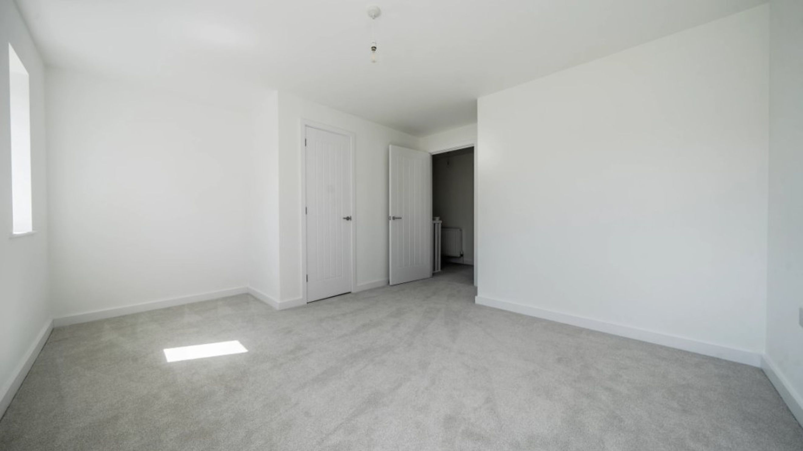 A bedroom with two doors, a window, and grey carpet.