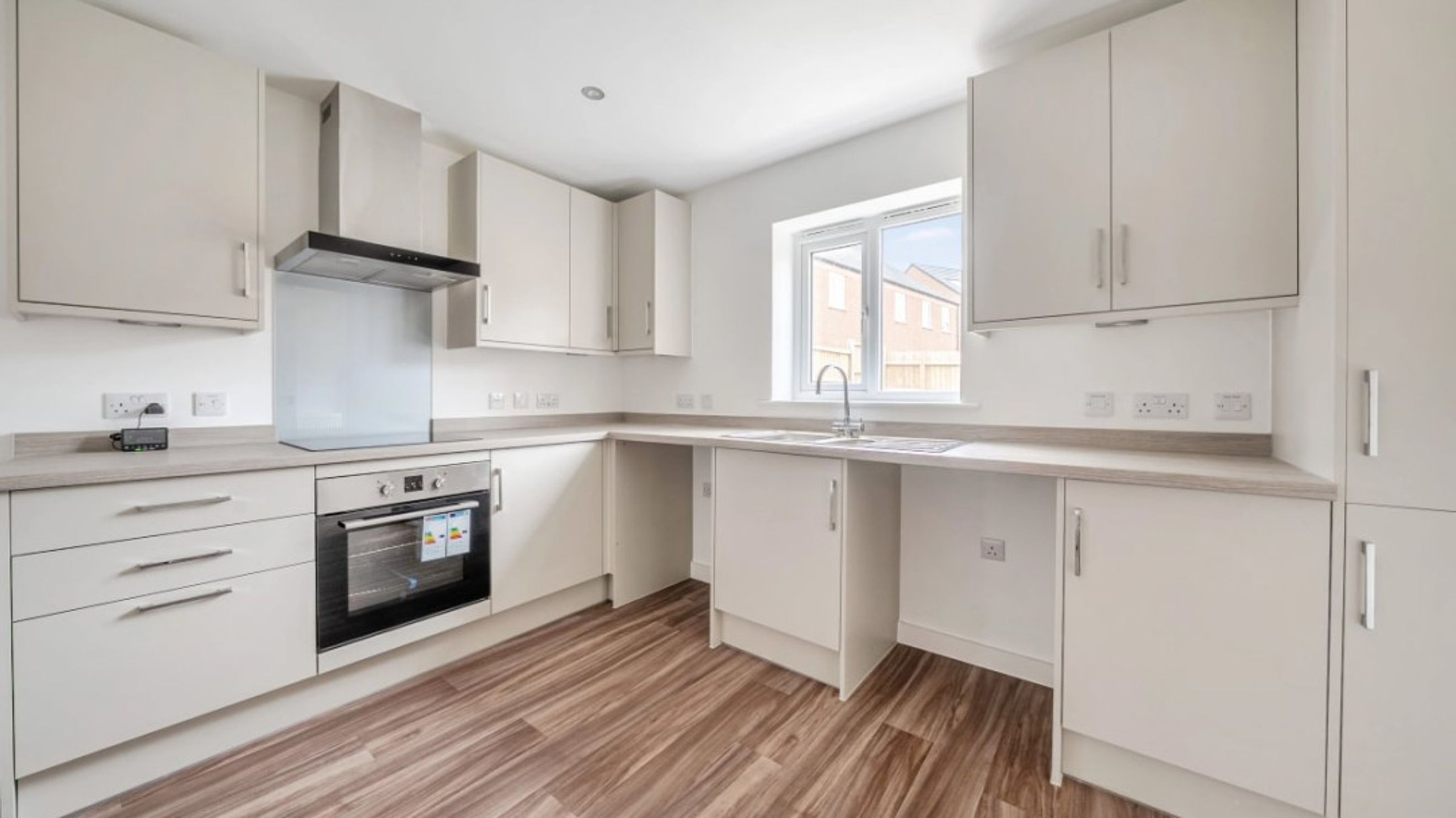 A modern kitchen with light-colored cabinets, a built-in oven, and a sink under a window.