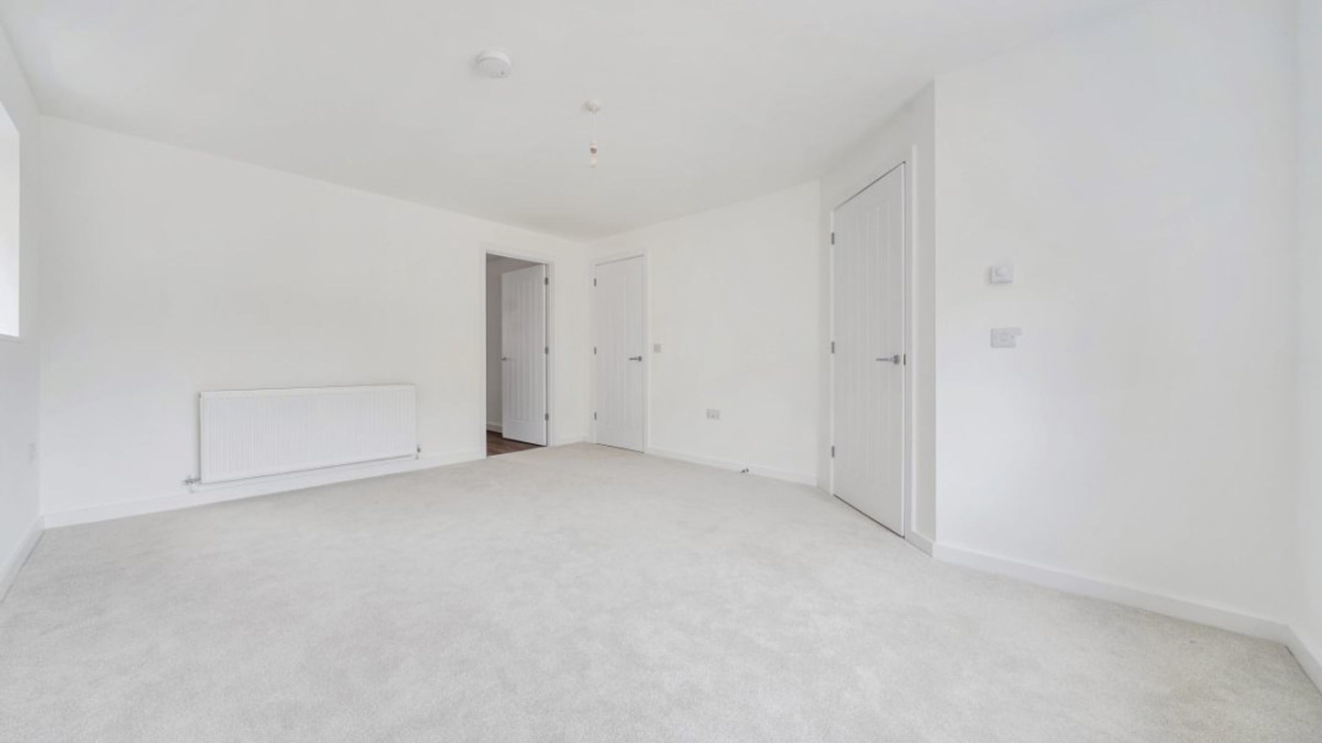 A spacious, empty room with white walls, light grey carpet, and white doors.