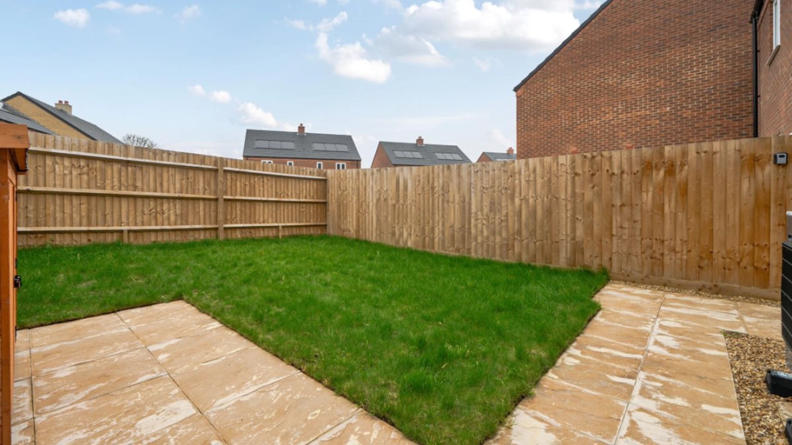 A backyard with a lawn, patio, and wooden fence.