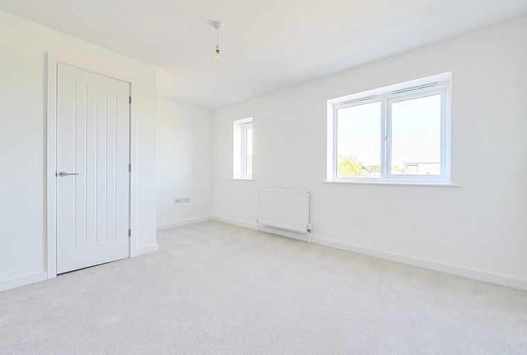 A bedroom with a white door, two windows, and a radiator.