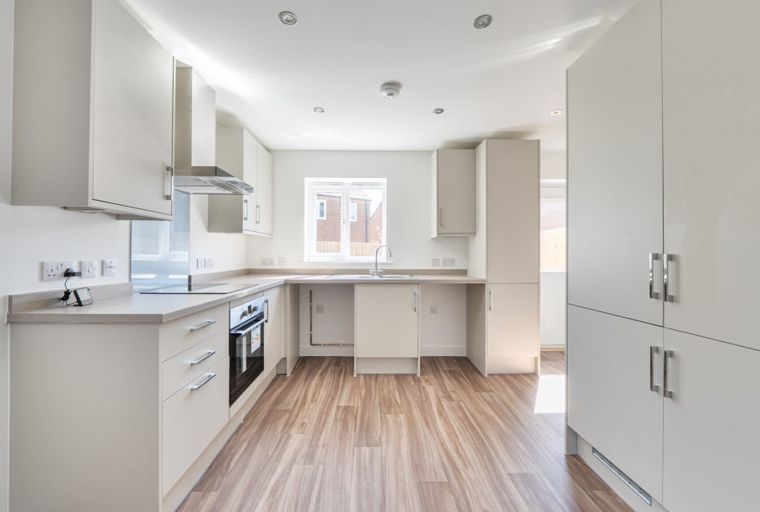 A modern kitchen with white cabinets, an oven, a sink, and a window.