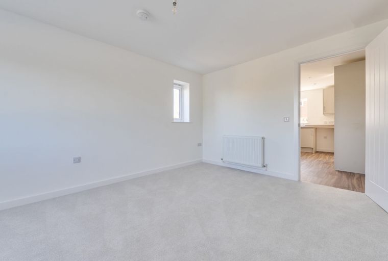 A bedroom with a window, radiator, and an open doorway leading to a kitchen.