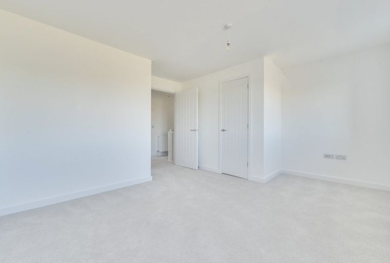 A spacious, empty room with white walls and light-colored carpeting.