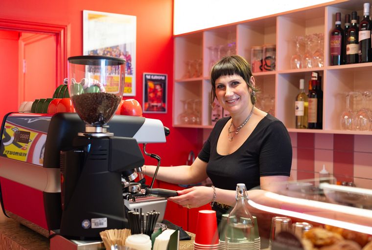 A woman smiling behind a coffee machine in a cafe.