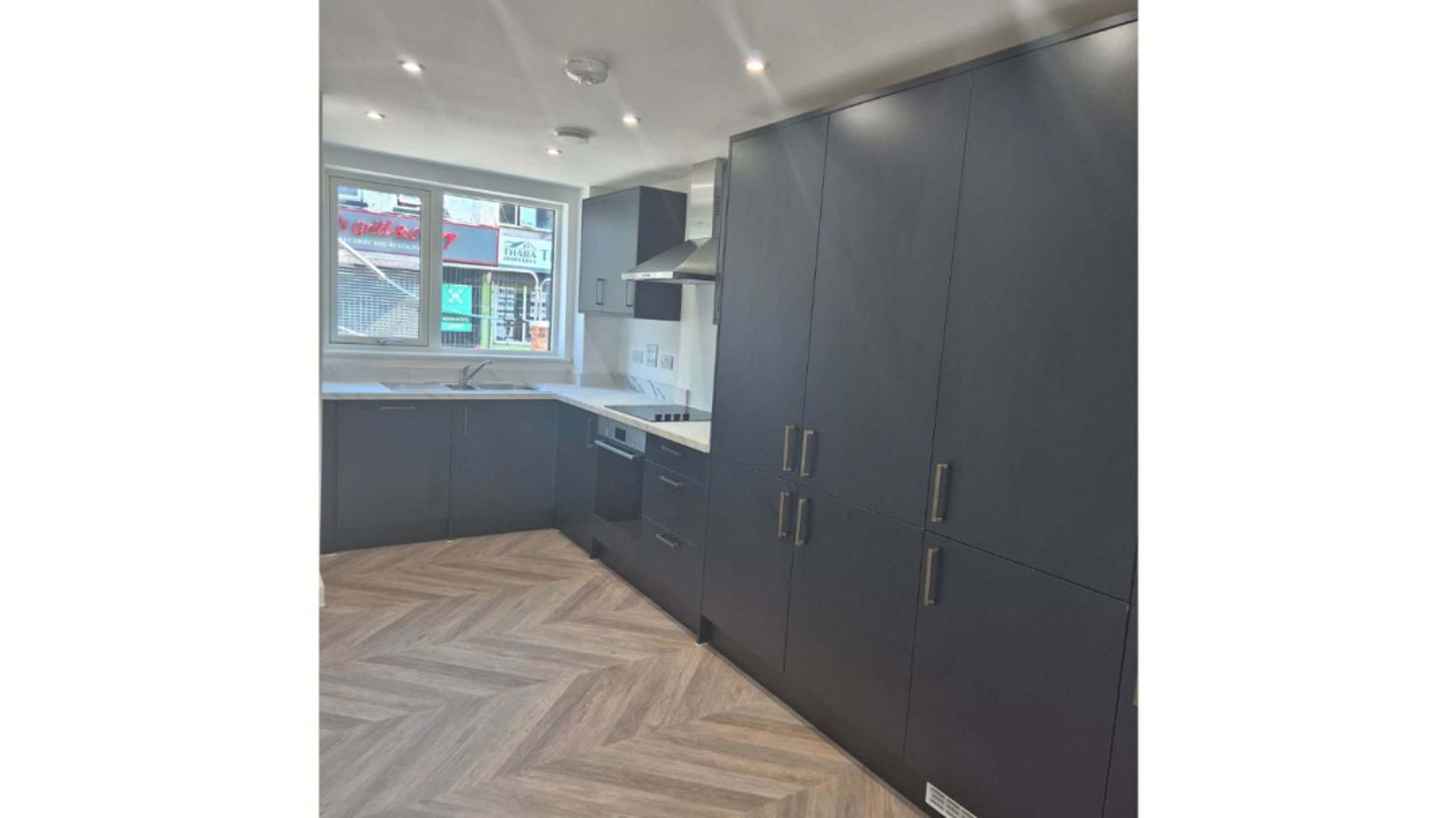 A modern kitchen with dark cabinets, a herringbone floor, and a window.
