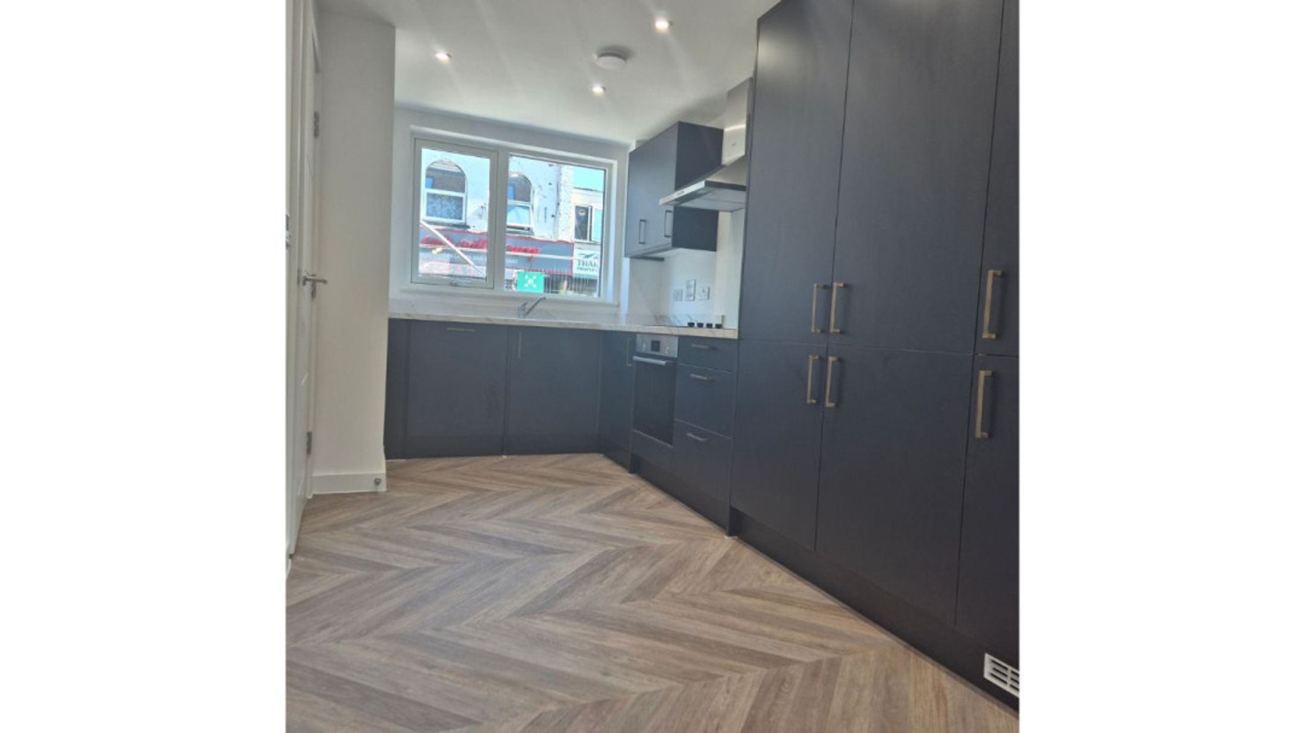 A modern kitchen with dark cabinets, a herringbone floor, and a window.