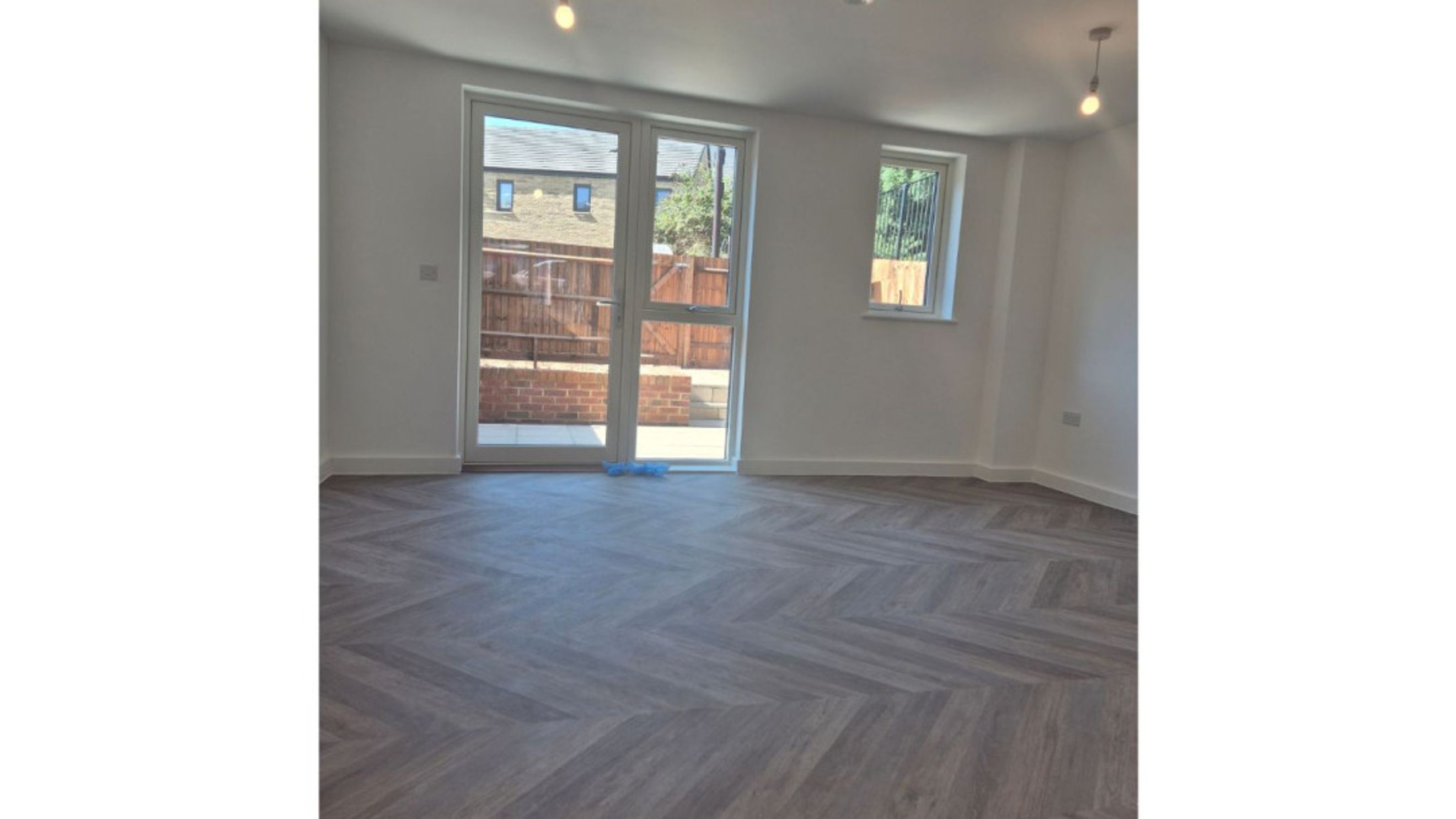 A living room with a herringbone floor and glass doors leading outside.