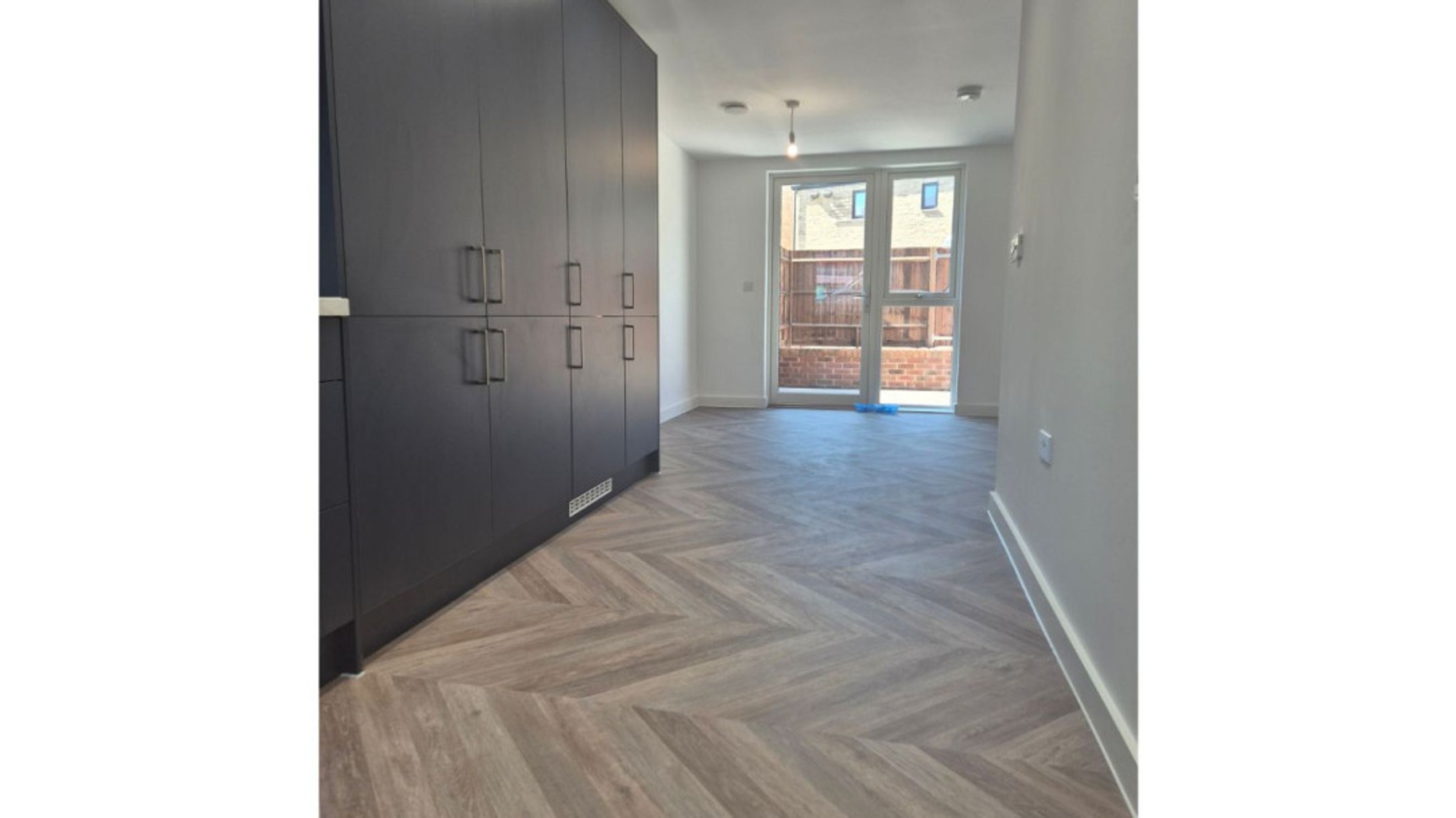 A hallway with dark cabinets and a herringbone floor leading to glass doors.